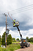 Electric worker in truck bucket near pole