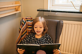Girl sitting in armchair and reading book at home