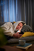 Kranker Mann auf dem Sofa liegend mit Smartphone