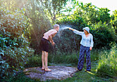 Woman in garden spraying man with garden hose