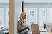 Lächelnde Frau hält Kaffeetasse im Büro