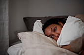Pensive young woman lying in bed and hugging pillow