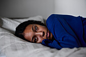 Pensive woman lying in bed at home