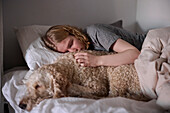 Crying young woman hugging dog in bed