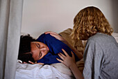 Young woman comforting friend lying in bed