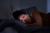 Pensive young woman lying in bed