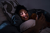 Smiling young woman using phone in bed