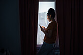 Young woman using phone by window