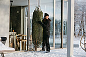 Woman carrying Christmas tree in front of house