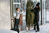 Frau mit Kindern beim Vorbereiten des Weihnachtsbaums vor dem Haus