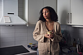 Pensive young woman standing in kitchen