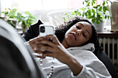 Young woman lying on bean bag and using phone