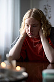 Pensive teenage girl sitting at table with head in hands