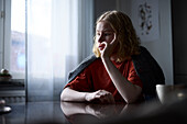 Pensive teenage girl sitting at table with hand on chin