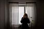 Teenage girl standing by window and drinking tea