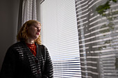 Pensive teenage girl looking through window