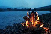 Metal kettle in campfire at dusk