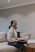 Smiling woman using laptop on sofa