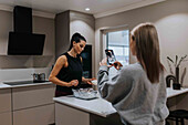 Woman in kitchen photographing friend preparing food