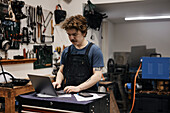 Schmied arbeitet mit Laptop in seiner Werkstatt