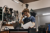 Schmied arbeitet mit Laptop und Dokumenten in seiner Werkstatt