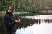 Junger Mann telefoniert mit Handy am See