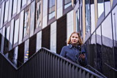 Young woman walking down stairs and using phone