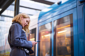 Frau mit Handy an einer Straßenbahnhaltestelle