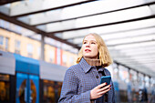 Frau mit Handy an der Straßenbahnhaltestelle