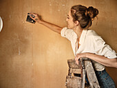 Woman on ladder scraping wall