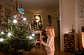 Kleines blondes Mädchen steht neben dem Weihnachtsbaum