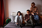 Children sitting on bed and using phones