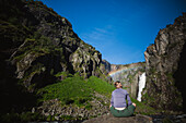 Rückansicht einer Frau mit Blick auf einen Wasserfall in den Bergen