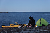 Man preparing food at sea, kayaks in background