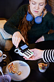 Junge Frau zahlt mit Telefon im Café