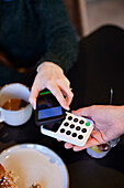 Junge Frau beim Bezahlen mit Telefon im Café