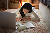Girl doing homework with laptop on floor in her bedroom