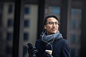 Handsome man with smartphone and paper cup on street