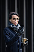 Schöner Mann mit Smartphone und Pappbecher auf der Straße