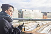 Handsome man with smartphone and paper cup on footbridge