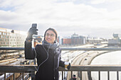 Gutaussehender Mann mit Smartphone macht ein Selfie auf einer Fußgängerbrücke