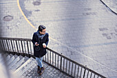 Hübscher Mann mit Smartphone und Pappbecher auf Stufen stehend