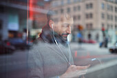 Eleganter Mann mit Smartphone, das sich im Fenster spiegelt