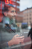 Eleganter Mann mit Smartphone, das sich im Fenster spiegelt