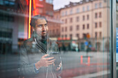 Eleganter Mann mit Smartphone, das sich im Fenster spiegelt