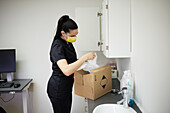 Female dentist in surgery putting supplies in cupboard