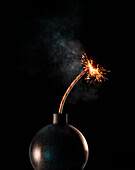 Black bomb with lit fuse against black background