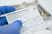 Close-up of hand in blue surgical glove holding covid-19 vaccination card