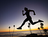 Silhouette of woman jumping on beach at sunset