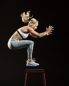Studio shot of athlete woman jumping over stool